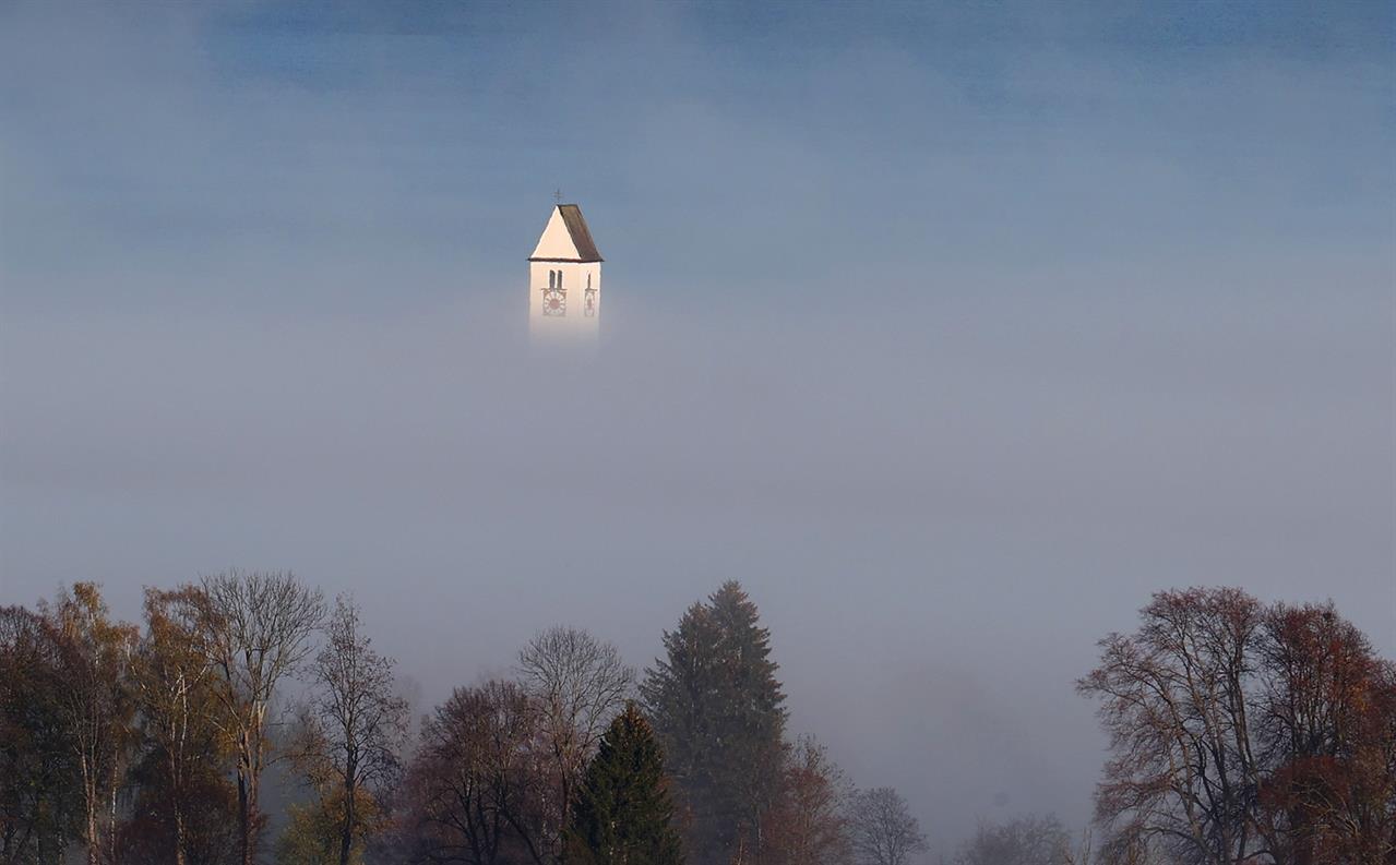 Kirchturm ragt aus Morgennebel